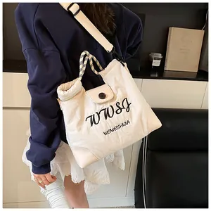 Detail of off-white canvas tote bag with black embroidery and woven rope handles