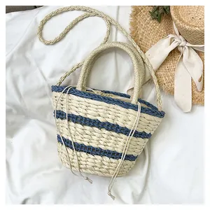 Détail du sac seau en paille tissée avec rayures bleues et fermeture à cordon sur tissu