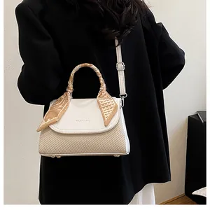 Detail of cream crossbody bag with woven texture and silk scarf wrapped on top handle