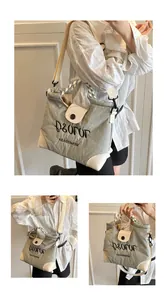 Detail view of large grey tote bag with embroidered letters and woven handle