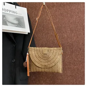 Detail of bohemian woven straw envelope bag with plush pompom and brown leather strap