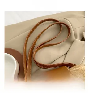 Detail der Strohtasche mit braunem Ledergriff und kontrastreichen weißen Nähten