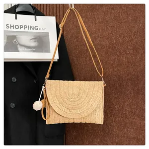 Detailed close-up of bohemian straw envelope bag with decorative tassel and shoulder strap