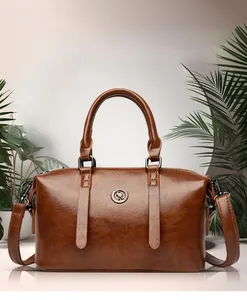 Detailed view of brown leather Boston bag with metallic emblem and detachable shoulder strap