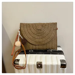 Detail of woven straw envelope bag with dual-tone pom-poms and leather strap