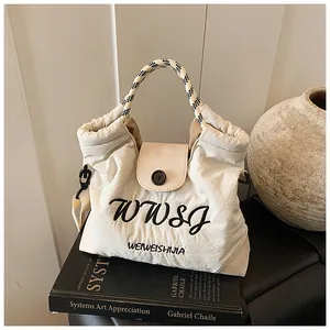 Detail of cream nylon tote bag with logo print and checkerboard woven handle on art books