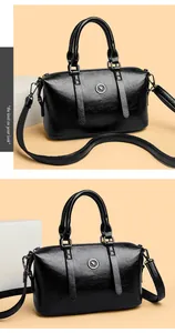 Detail of glossy black faux leather boston bag with kangaroo logo and crossbody strap