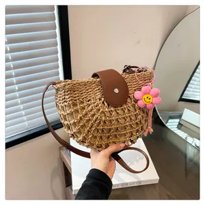 Detail van halfronde rieten tas met bruine leren riem en roze zonnebloem hanger decor