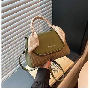 Detail of dark green handbag featuring woven texture and silk scarf wrapped handle