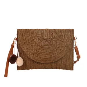 Bohemian woven straw envelope bag in brown with plush pompons and faux leather strap