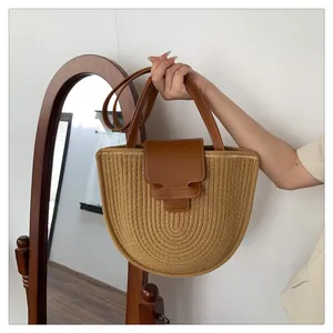 Detail einer halbrunden Strohtasche mit braunen Ledergriffen und dekorativem Verschluss