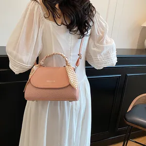 Pink crossbody handbag with woven texture and decorative silk scarf handle on model