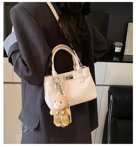 Detail der cremeweißen Kunstledertasche mit silbernem Drehverschluss und Plüschbär-Anhänger