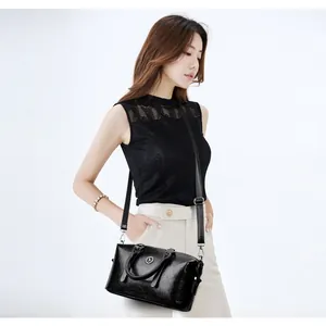 Chic black soft leather shoulder bag with circular metal logo and adjustable strap