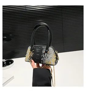 Detail of mini shell bag with snake skin pattern, black handles and gold ball chain strap