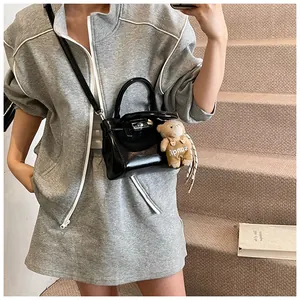 Details einer schwarzen Lackledertasche mit Silberverschluss und Plüschbär-Anhänger