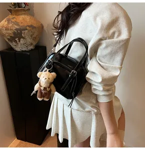 Modello con borsa a tracolla nera lucida e un simpatico ciondolo a forma di orsetto