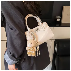 Detail der cremefarbenen Tasche mit silbernem Drehverschluss, Plüschbär und Dekoschal