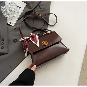 Detail of burgundy leather handbag featuring metal twist lock and decorative silk scarf