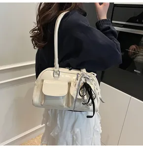 Dettaglio della borsa Boston in vernice crema con ciondoli decorativi e due tasche frontali