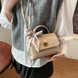 Beige structured crossbody bag with silk scarf and gold ring lock held by a model