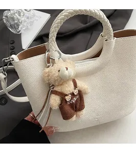 Detailansicht einer weißen Eimer-Tasche mit gewebtem Griff und Plüschbär-Anhänger
