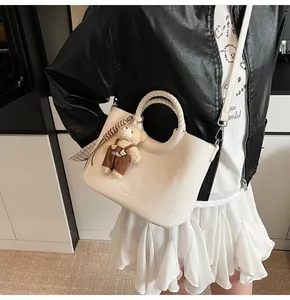 Witte lederen bucket bag met geweven handvat en schattige beer hanger getoond op model