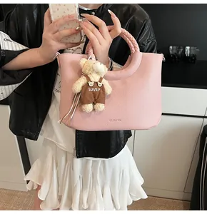 Detail van roze leren handtas met gevlochten handvat en een pluche beer hanger