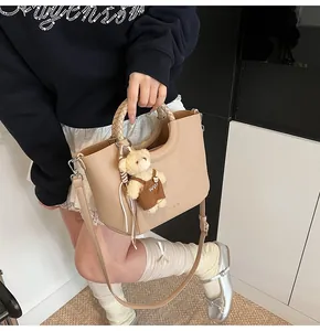 Detail van de abrikooskleurige leren handtas met geweven handvat en teddybeer-accessoire