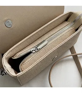 Détail de la fermeture éclair argentée et de la texture tissée du sac à bandoulière beige