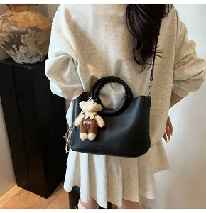 Detail van zwarte lederen emmer tas met gevlochten handvat en schattige teddybeer