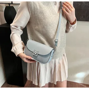 Detail of light blue saddle bag featuring woven texture and silver geometric metal clasp