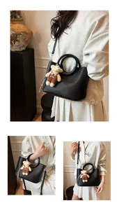 Detail van zwarte bucket bag van generfd leer met gevlochten handvat en een beerhanger