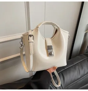 Detalle de bolso cubo crema con hebilla cuadrada plateada y textura de cuero liso