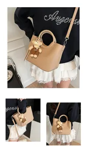 Detail van beige emmertas met gevlochten handvat, kiezelleder en pluche berenhanger