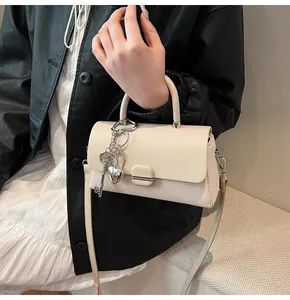 Détail du sac crème avec textures mixtes, boucle métallique et breloque en forme de cœur