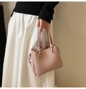 Detail of pink lychee leather handbag featuring knotted dual handles and metal D-rings