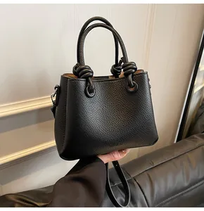 Detailed close-up of black lychee grain leather bucket bag with unique knotted rope handle