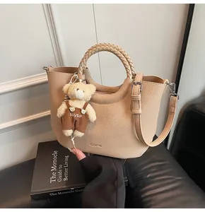 Detail van beige handtas met geweven handvat en schattig beer-accessoire als hanger