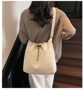 Détail du sac seau en nylon crème avec fermeture à cordon et bandoulière large sur modèle