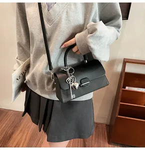 Détail du sac à rabat noir avec breloque cœur argentée et texture en cuir lisse