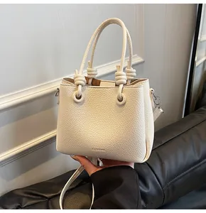 Detail of cream lychee leather bucket bag with decorative knots and silver hardware