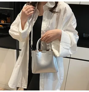 Detail of silver metallic tote bag featuring cylindrical handles and a detachable shoulder strap