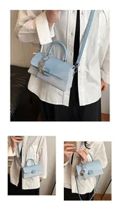 Détail du sac à main bleu clair avec texture tissée, breloque coeur et rabat en cuir lisse