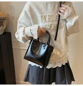 Detail of glossy black leather handbag with round handle and silver metal hardware