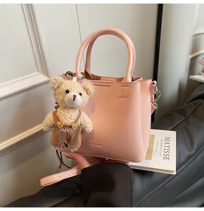 Detail of pink faux leather crossbody bag featuring a cute brown bear charm and logo