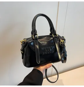 Dettaglio della borsa nera lucida con lettere a rilievo e accessori in metallo dorato