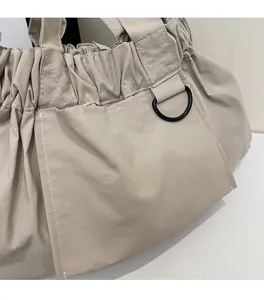 Detail of soft beige fabric shoulder bag showing pleated texture and black metal D-ring