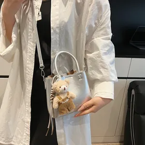 Silver metallic tote bag with plush bear charm and detachable strap on white shirt model