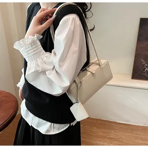 Borsa sottobraccio beige minimalista con piccolo ciondolo mostrata indossata in una scena di vita